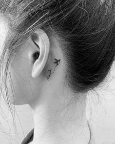 a woman's ear has a small bird tattoo on it