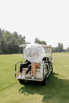 two women sitting on the back of a golf cart with an umbrella over their heads