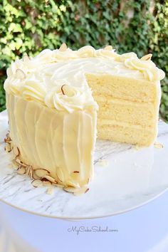 a cake with white frosting sitting on top of a table next to a green bush