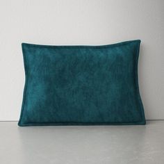 a green velvet pillow sitting on top of a white floor next to a gray wall