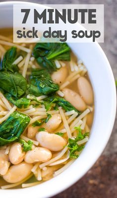 a white bowl filled with noodles and spinach on top of a table next to a cup of soup