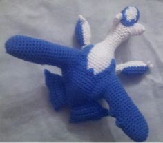 a crocheted blue and white stuffed animal laying on top of a bed covered in sheets