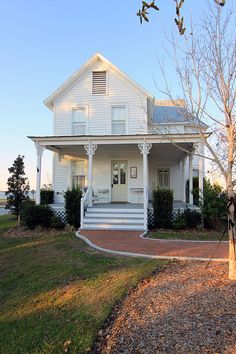 a white house sitting on top of a lush green field next to a tree in front of it