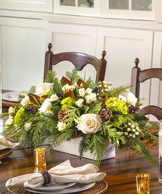 a dining room table set for christmas with white flowers and greenery in the center