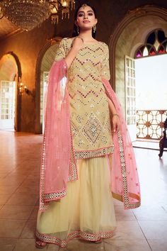 Exuding elegance and finished with perfection, this pale yellow organza sharara suit which will make your look very subtle yet edgy.This round neck and elbow sleeved party wear suit designed with mirror and thread work.Teamed up with net sharara pant in pale yellow color with pink net dupatta.Sharara pant has mirror and thread work.Dupatta highlighted with sequins, mirror and thread work.This sharara suit can be customised up to maximum size available in inches 58.Slight color variation may occur due to photographic reasons. Pink Gharara, Wedding Sharara, Bridal Sharara, Gharara Suits, Organza Suits, Organza Top, Sharara Suit, Party Kleidung, Net Dupatta