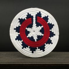 a red, white and blue woven basket sitting on top of a wooden table next to a black wall