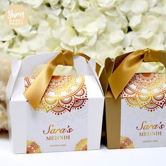 two white boxes with gold ribbons on them sitting next to some flowers and a teddy bear