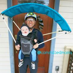 a man holding a baby in a sling on the front steps of a house while wearing skis