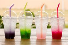 four different colored drinks are lined up on a table with their straws sticking out