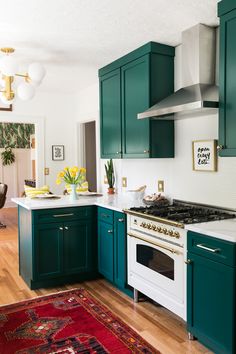 a kitchen with green cabinets and an area rug on the floor in front of the stove