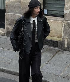 a woman in a black hat and jacket is walking down the street with her hand on her hip