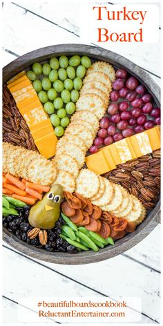 a platter filled with crackers, grapes, cheese and olives for a turkey board