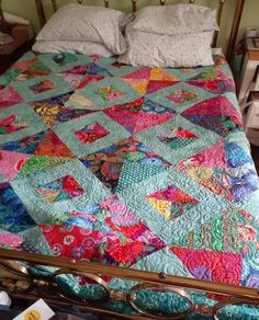 a bed with a colorful quilt on top of it next to a pair of glasses