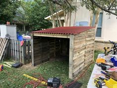 a wooden shed with a red roof and some tools on the ground next to it