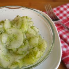 a white bowl filled with cucumbers on top of a red and white checkered table cloth