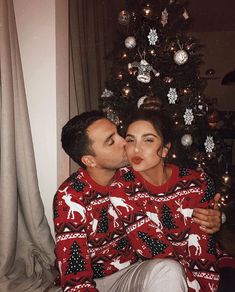 a man and woman kissing in front of a christmas tree wearing ugly sweaters with reindeer print on them