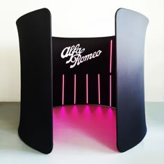 a black and pink stand with neon lights on it's sides, in front of a white wall