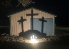 the shadow of two crosses is projected on the ground in front of a small building