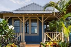 a small blue house surrounded by trees and plants in front of the door is a porch with steps leading up to it