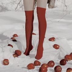 a woman standing on top of a pile of apples in the snow with red socks