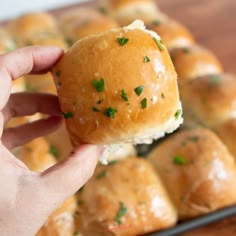 a hand holding up a small roll with cheese and herbs on it