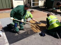 three men in green jackets are working on the pavement