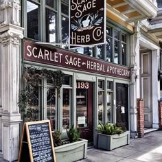 the front of a store with plants and signs on the side of it's windows