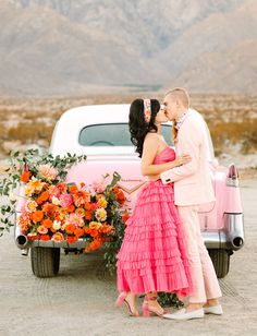 a man and woman kissing in front of a pink car with flowers on the bed