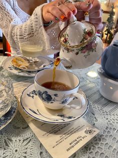 a woman pouring tea into a cup on top of a table