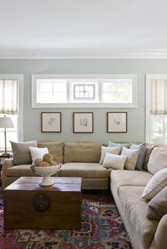 a living room filled with furniture and pillows on top of a carpeted floor next to two windows