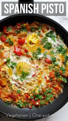 a skillet with eggs, tomatoes and parsley in it on a white table