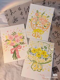 three cards with flowers on them sitting on a bed