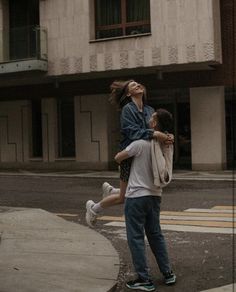 a man carrying a woman on his back while walking down the street in front of a building