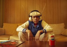 a man sitting on top of a wooden table wearing headphones and holding a can of soda