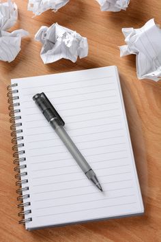 a notepad with a pen on top of it next to crumpled up paper balls