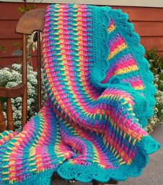 a crocheted blanket sitting on top of a wooden chair next to a flower garden