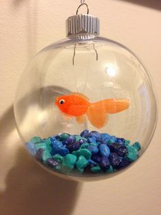 a glass ornament with an orange fish in it and some blue rocks on the bottom