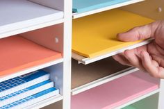 a hand is picking up some colored folders from a bookshelf with two hands