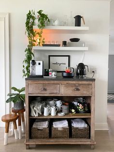 a wooden cabinet filled with dishes and cups on top of a hard wood floor next to a potted plant