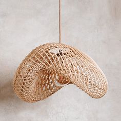 a rattan light hanging from a rope on a wall in a room with concrete walls