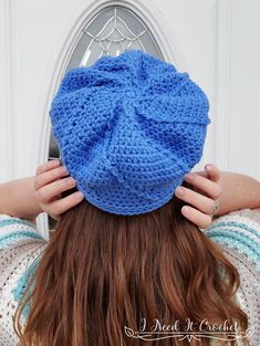 a woman wearing a blue crochet beanie with her hands on her head