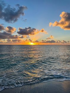 the sun is setting over the ocean with clouds in the sky and waves on the beach