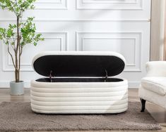 a white ottoman sitting on top of a rug next to a chair and potted plant