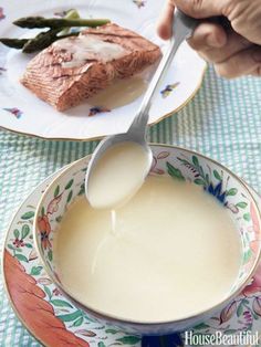 a person is spooning milk into a bowl with food on the plate next to them