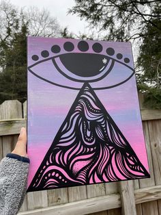 a person holding up a piece of art with an eye painted on it's side