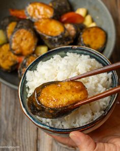 someone holding chopsticks over rice in a bowl with other food on the side