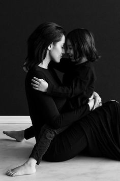 two women sitting on the floor hugging each other with their arms around one another while they both wear black clothing