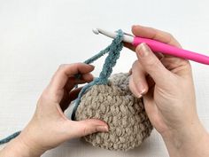 two hands crocheting the ends of a ball of yarn with a pink needle