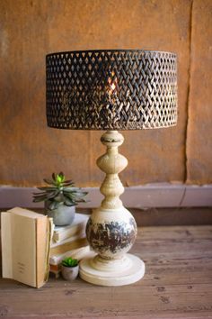 a lamp sitting on top of a wooden table next to a book and potted plant