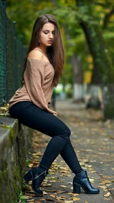 a beautiful young woman sitting on top of a stone wall